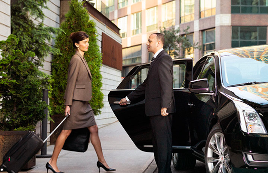 woman walking towards a waiting car with door help open by chauffeur